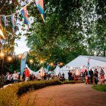 A large marquee in the background, hedges, festoon lighting, colourful flags set the scene for an incredible corporate summer event